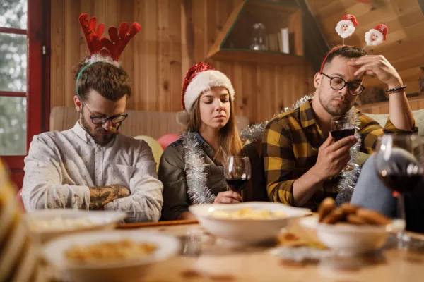 Three people in festive attire sit at a table with food, looking bored or contemplative.