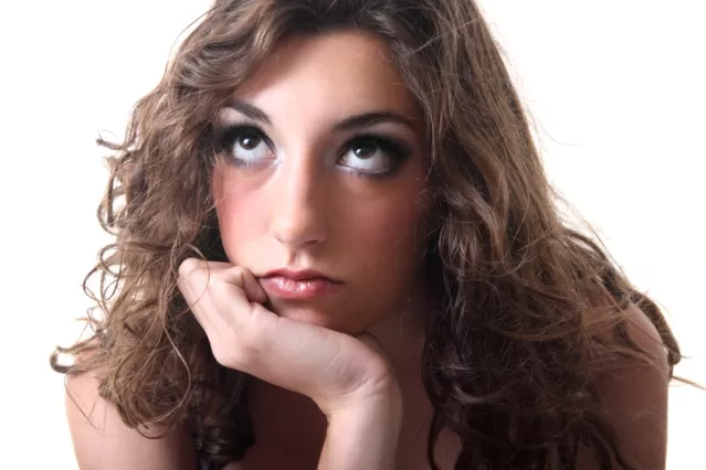 A young woman rests her chin on her hand, looking thoughtfully upward with a neutral expression.