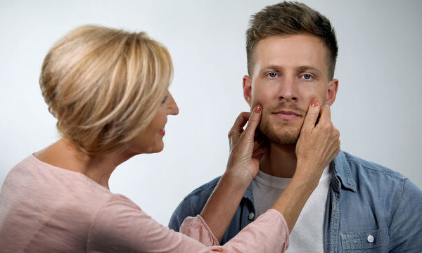 A woman gently holds a man's face, examining him closely.