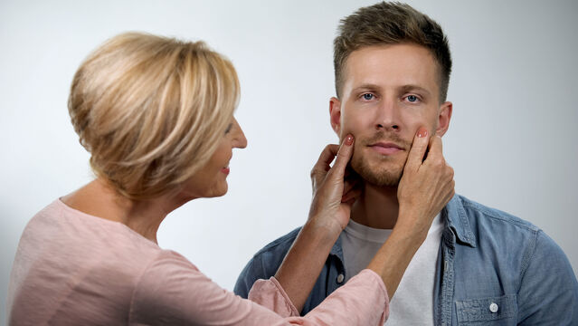 A woman gently holds a man's face, examining him closely.